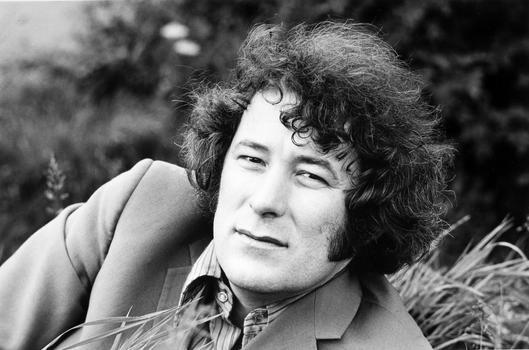 A portrait of Seamus Heaney, with him reclining in a field 